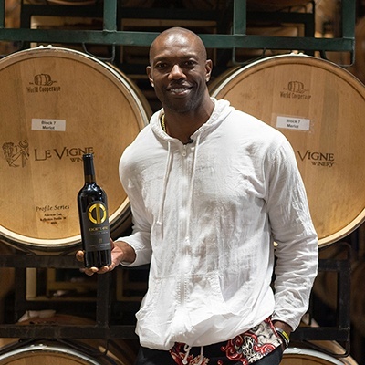 A man holding a bottle of wine in front of barrels.